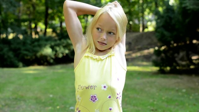 little lively girl stretchs her arms and neck in the park - workout 