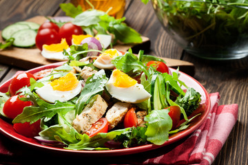 Fresh salad with chicken, tomatoes, eggs and arugula on plate