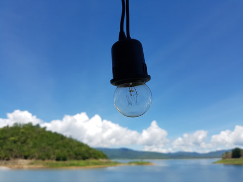 Empty black light bulb with ocean lake and bright blue sky on background