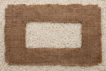 Fototapeta na wymiar Frame made of rough burlap lies on rice grains