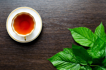 natural herbal antipyretic - organic raspberry leaves tea

in a white porcelain сup with fresh green leaves on a dark wooden table, shot at an angle of 90 degrees, for labels, packages, menus, etc
