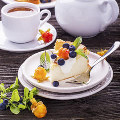 Homemade breakfast. Fresh cheesecake with Nordic berries cloudberries and blueberries in plain wooden background served  cloudberry tea in a white ceramic bowl. Decorated branches forest 