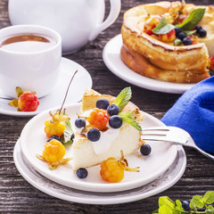 Homemade breakfast. Fresh cheesecake with Nordic berries cloudberries and blueberries in plain wooden background served  cloudberry tea in a white ceramic bowl. Decorated branches forest 