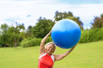 Happy senior woman with stability ball over head
