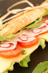 sandwich French baguette, cheese, ham, tomato, radish, lettuce closeup. homemade food. crisp bread