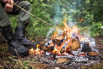 A man warms himself by the fire in the forest, rain, autumn