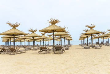 Thatched umbrellas and wooden lounge chairs on the beach.