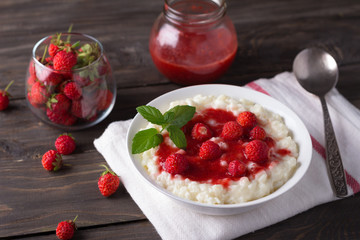 Creamy rice pudding with strawberry jam and fresh strawberries on a wooden table