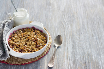 Homemade cherry crumble with oatmeal and almonds with yogurt on a light wooden table 