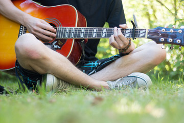 Junger Mann sitzt gitarrespielend im Park, Ausschnitt