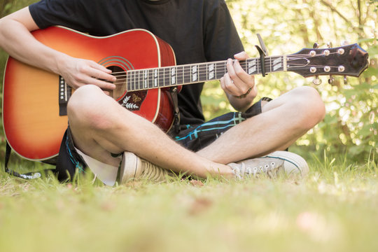 Junger Mann sitzt gitarrespielend im Park, Ausschnitt