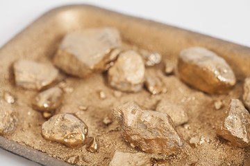 Golden nuggets on grungy wash pan with sand on white background