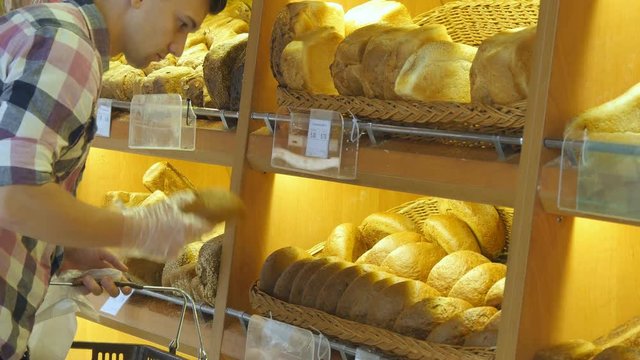 Man chooses a fresh bread loaf in the supermarket. Young guy taking a loaf of bread from the shelf and smelling it. Shopping in the grocery