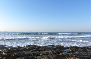 Fototapeta na wymiar Dark Rocks Ocean Waves and Blue Skyline Seascape
