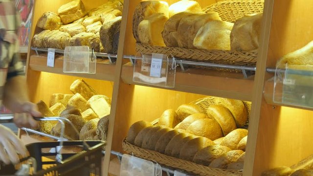 Man chooses and putting a fresh bread loaf into a package in the supermarket. Young guy taking a loaf of bread from the shelf and putting it into the basket. Shopping in the grocery