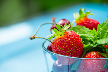 Glass with ripe cherry and strawberry on the blue wooden table