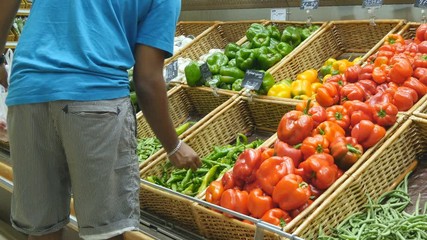 Indian man is choosing peppers in a grocery supermarket. Guy  selecting fresh ripe green peppers in grocery store produce department. Rear view