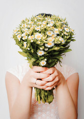 Girl with bouquet of camomile at white wall