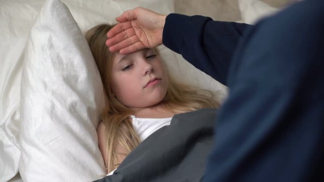 Young caucasian female sick in bed with mother checking for a fever. 