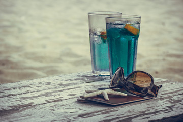 Concept for vacation, travel, summer holiday sea and ocean tranquility and relaxation. Cocktails in blue on the beach table with two passports starfish and sunglasses with sand beach background