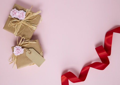 Birthday Gifts Wrapped In Brown Paper With Flowers And Red Silk Ribbon On A Pink Background
