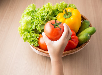 Tomato on hand with fresh vegetable prepared in bowl on wooden t