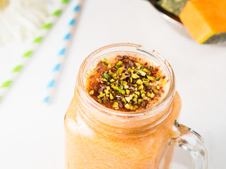 Pumpkin and banana vegan smoothie with soy milk, flax seeds, ginger and orange juice, with pistachio topping, on rustic wooden table. Healthy breakfast still life. Closeup