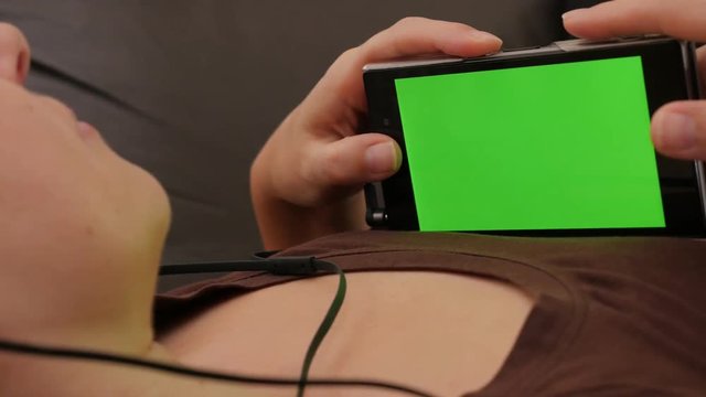 Headphones attached on smart phone in woman hands with green screen 4K 2160p UHD slow panning footage - Woman holding mobile in hands while listening to music 4K 3840X2160 UHD panning video 