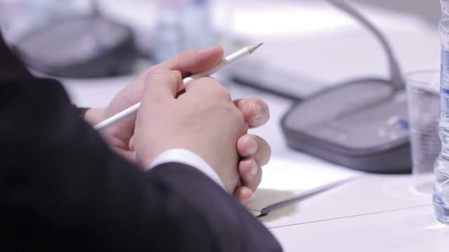The politician at the meeting holding a pencil, periodically writes important theses. Next to the microphone stand. International Forum.