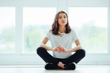 Lost in thoughts. Young beautiful brunette hipster woman sitting on floor near huge window and looking away