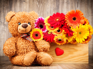 Obraz premium Beautiful flowers and a teddy bear on wooden background