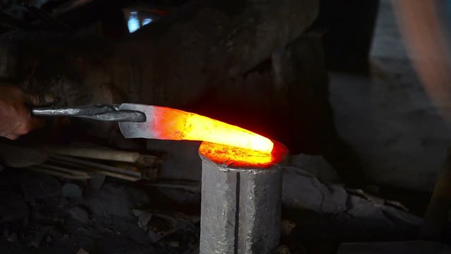 Team of local laborers using traditional methods and tools to shape a piece of red hot steel on an improvised anvil, in a blacksmith shop, with sound. Video 1920x1080