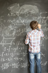 Boy with chalk writting complicated math formulas on black board
