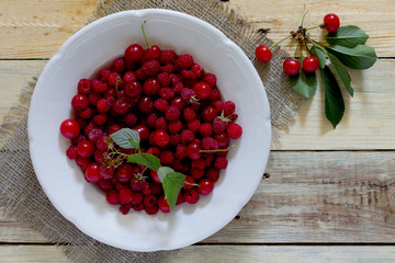 Ripe sweet cherries and raspberries in a bowl on a wooden table,
