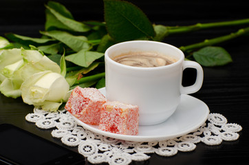 Mug of coffee with milk close-up, oriental sweets. smartphone, white roses on a black background