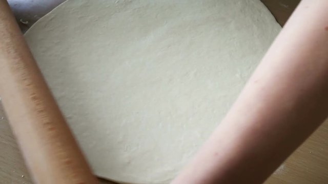 Rolling dough with hands and wooden roller on table
