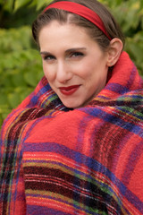 Portrait of a woman in her 30's wrapped in a red plaid blanket.