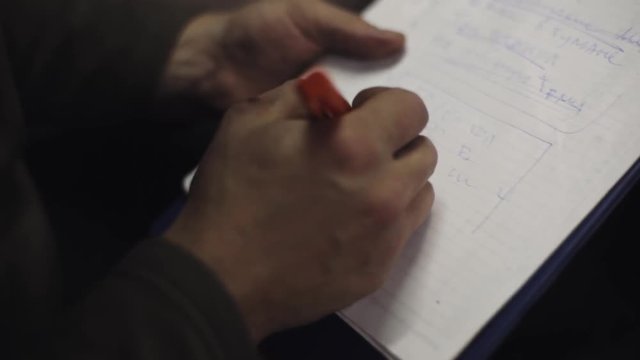 Man sit on chair writing words in list on sheet of paper in folder by blue pen. Planning