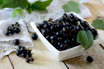 Ripe berries of a black currant in a bowl on a wooden table, sel
