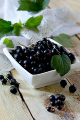 Ripe berries of a black currant in a bowl on a wooden table, sel