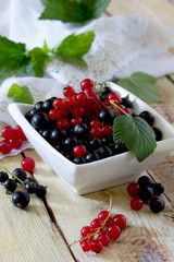 Ripe berries are black and red currants in a bowl on a wooden ta