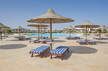 Sunbeds and parasols by a tropical hotel resort swimming pool