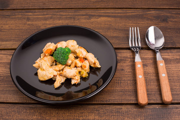 chicken, broccoli on a black plate with a spoon and a plate. wooden rustic table