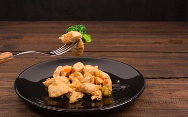 chicken, broccoli on a black plate with a spoon and a plate. wooden rustic table
