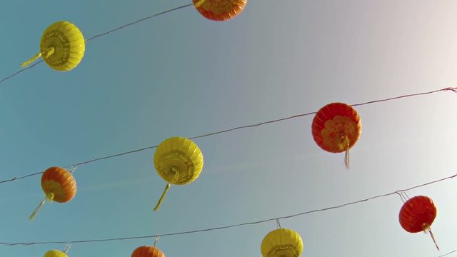 Neat rows of traditional, tasseled, Chinese paper lanterns in red and yellow, hanging from wires outside an urban Buddhist temple in Southeast Asia.