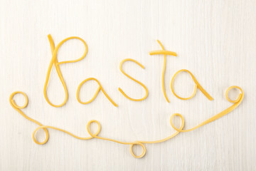 Word PASTA made of cooked spaghetti on wooden background