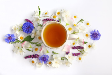 Fototapeta na wymiar Cup of tea with fresh flowers lying around on white background