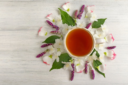 Cup of tea with fresh flowers lying around on wooden background