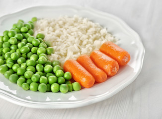 Cooked rice with baby carrots and green pea in white plate on table