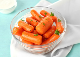 Small baby carrots in glass bowl on light blue background
